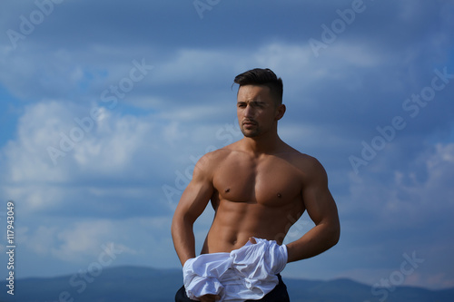 Sexy muscular man undressing on sky background