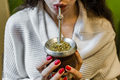 Young woman drinking traditional Argentinian yerba mate tea from a calabash gourd with bombilla stick. Selective focus.