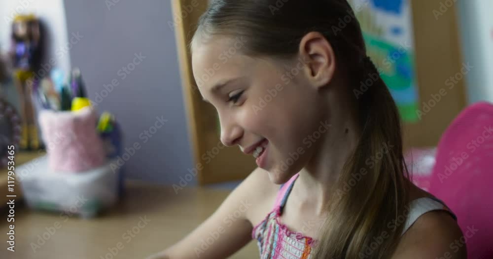 Little smiling schoolgirl sitting with smartphone playing games at desk in nursery Little smiling schoolgirl sitting with smartphone playing games at desk in nursery