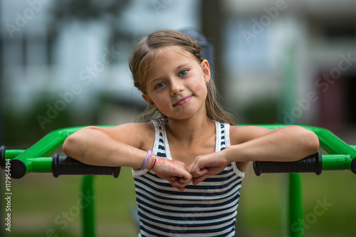 Portrait of little girl sitting on exercise equipment in the public park.