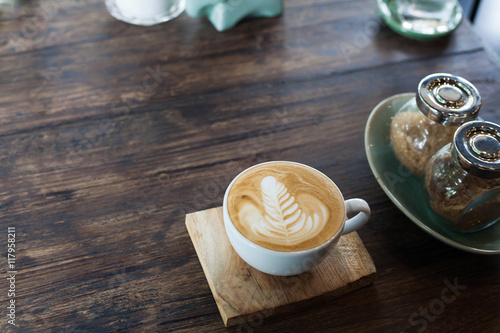 A cup of coffee with heart pattern in a white cup on wooden background