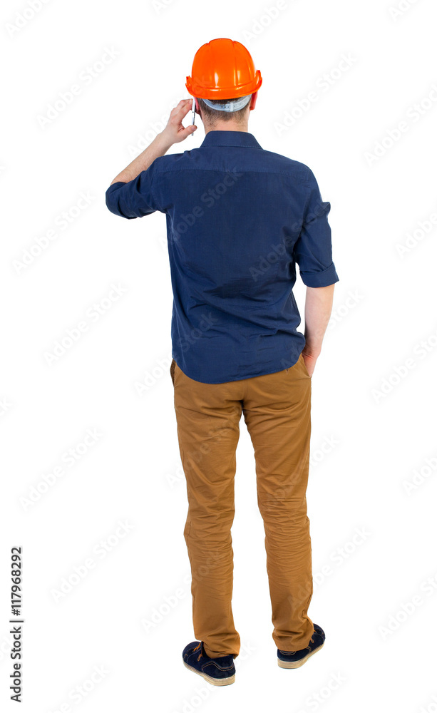 Backview of business man in construction helmet stands and enjoys tablet or using a mobile phone. Standing young guy. Rear view people collection. backside view of person. Isolated over white Backview of business man in construction helmet stands and enjoys tablet or using a mobile phone. Standing young guy. Rear view people collection. backside view of person. Isolated over white