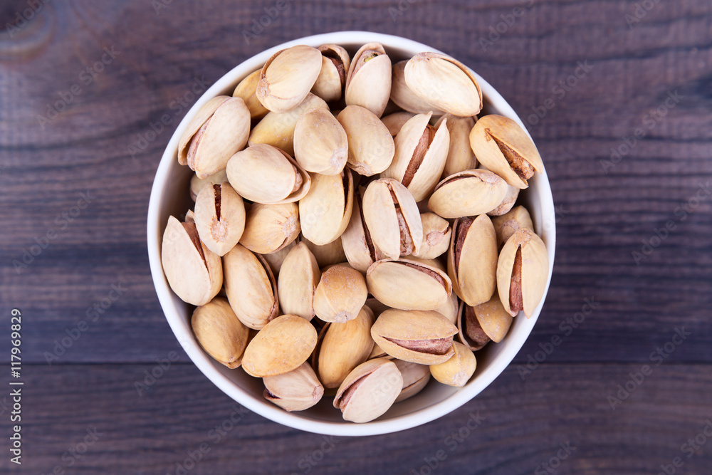 Salted pistachios in a bowl on dark wooden table. Top view with copyspace Salted pistachios in a bowl on dark wooden table. Top view with copyspace