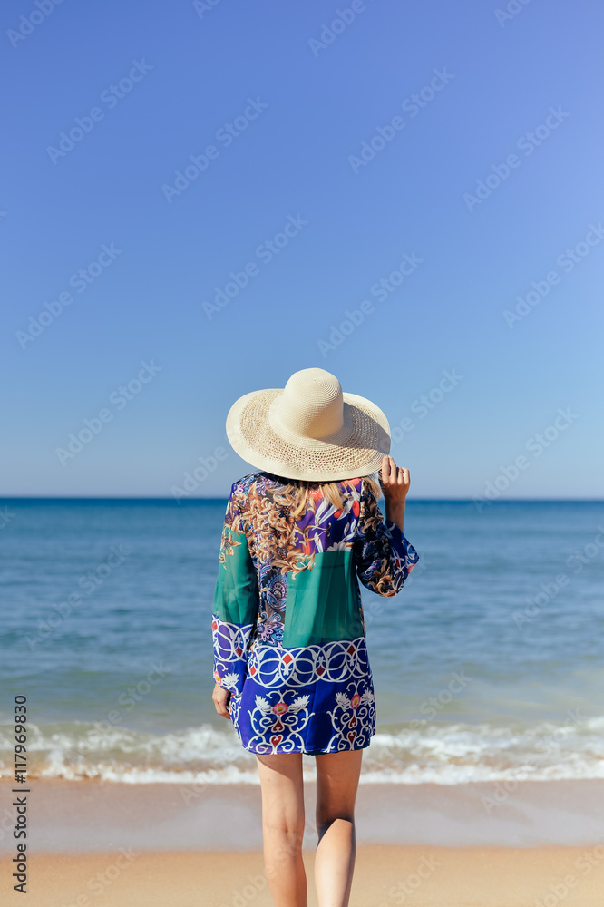 Rear view of romantic young lady wearing dress hat on sunny tropical beach background. Summer vacation