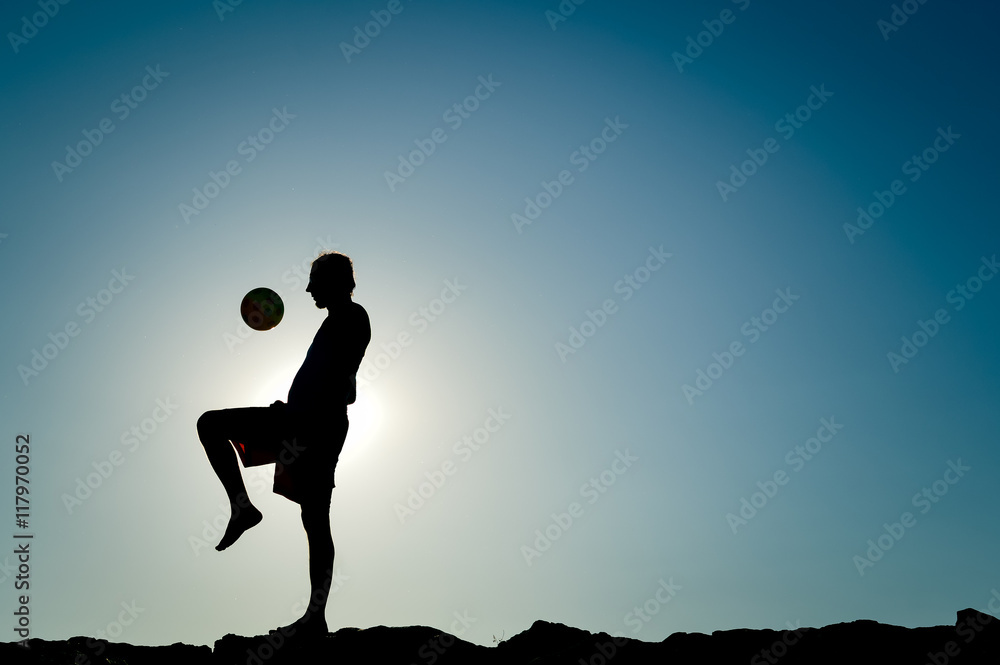 Male silhouette at dawn, player kicking ball, sunny blue sky background outdoors