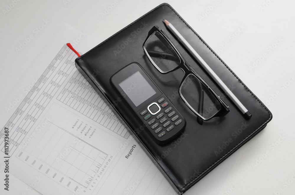 The document of the report. Glass, phone and pen on notebook. The document of the report. Glass, phone and pen on notebook.