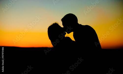 Silhouettes of a man and woman kissing passionately in yellow an
