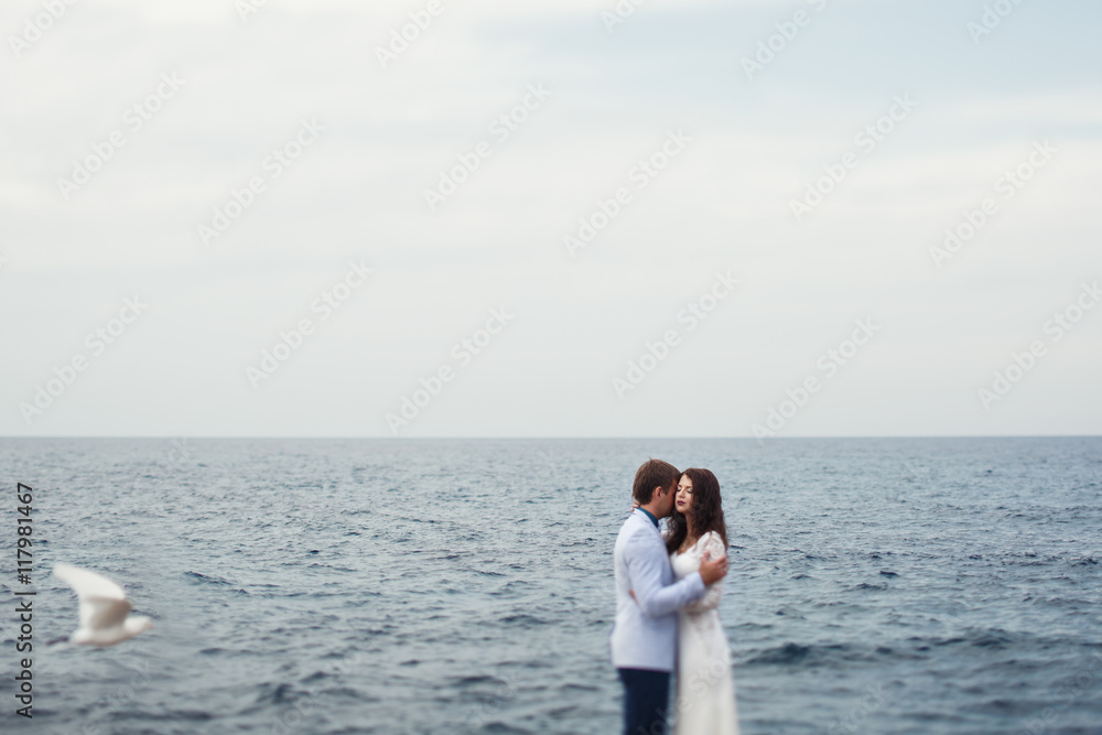 Gulls fly around the wedding couple standing by the blue sea Gulls fly around the wedding couple standing by the blue sea
