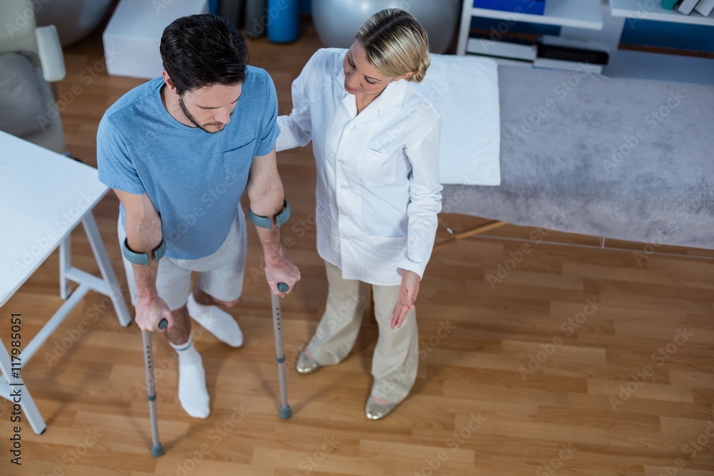 Physiotherapist helping patient to walk with crutches Physiotherapist helping patient to walk with crutches