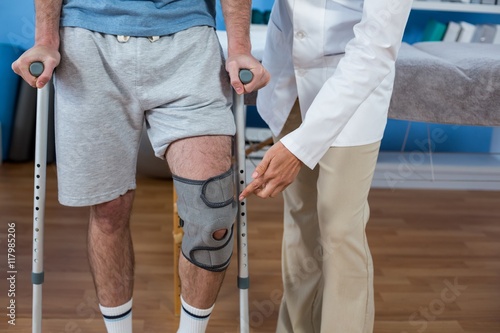 Foto Physiotherapist helping patient to walk with crutches