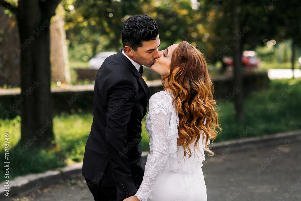 Groom kisses bride with long curls holding her hand tightly Groom kisses bride with long curls holding her hand tightly
