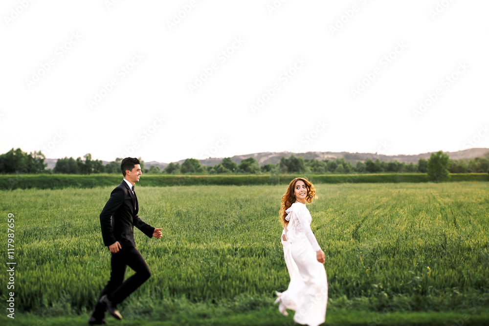 Groom tries to catch a bride running around green field Groom tries to catch a bride running around green field