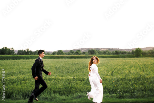 Groom tries to catch a bride running around green field