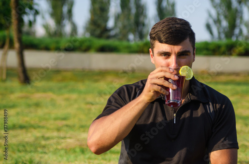 The man sits on a grass and drinks smoothie.