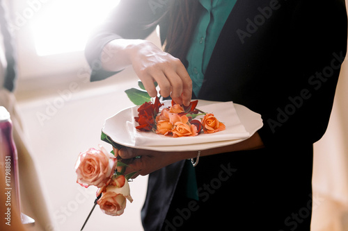 Woman puts delicate orange rose buds on the white plate