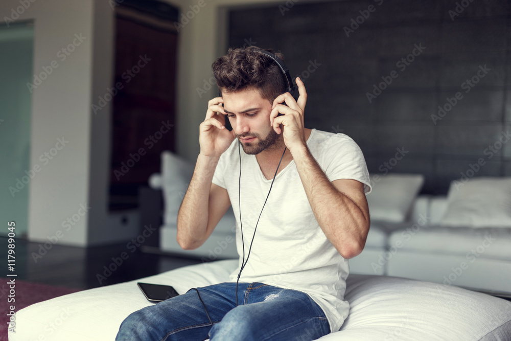 Obraz premium Young bearded hipster guy listening music indoor on tablet