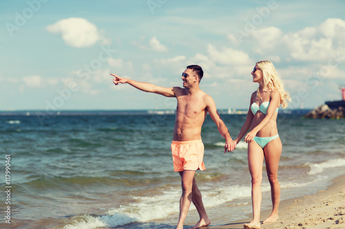 happy couple in swimwear walking on summer beach