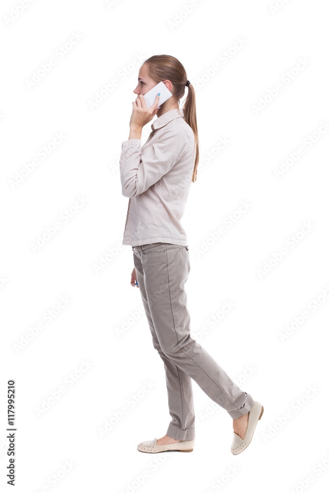 side view of a woman walking with a mobile phone. back view ofgirl in motion. backside view of person. Rear view people collection. Isolated over white background. A girl in a white jacket is side view of a woman walking with a mobile phone. back view ofgirl in motion. backside view of person. Rear view people collection. Isolated over white background. A girl in a white jacket is