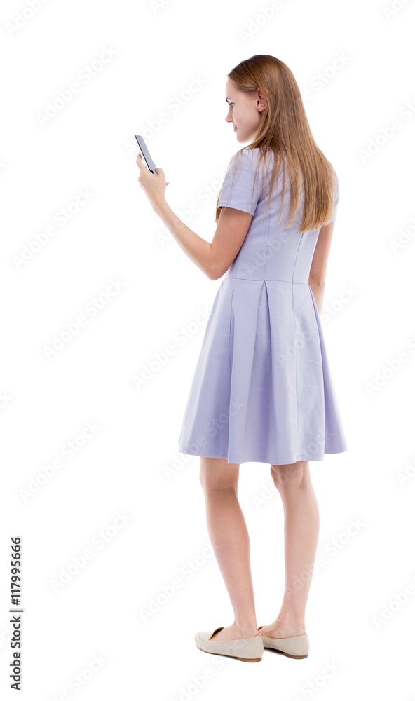 back view of standing young beautiful woman and using a mobile phone. girl watching. Rear view people collection. backside view of person. Isolated over white background. The girl in a blue dress back view of standing young beautiful woman and using a mobile phone. girl watching. Rear view people collection. backside view of person. Isolated over white background. The girl in a blue dress