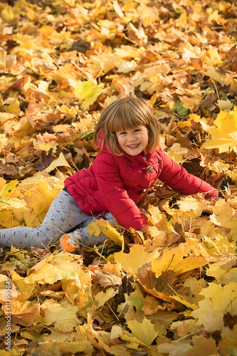 Baby girl playing with yellow leafs in autumn