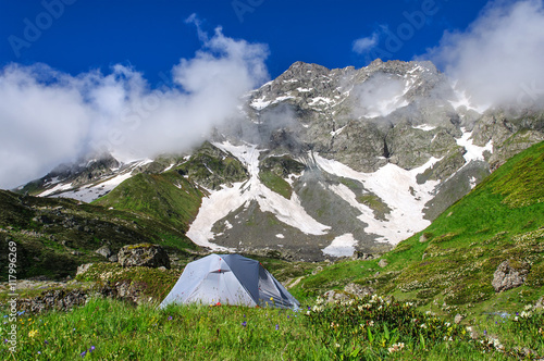 gray tent in grass on background of mountains and rocks