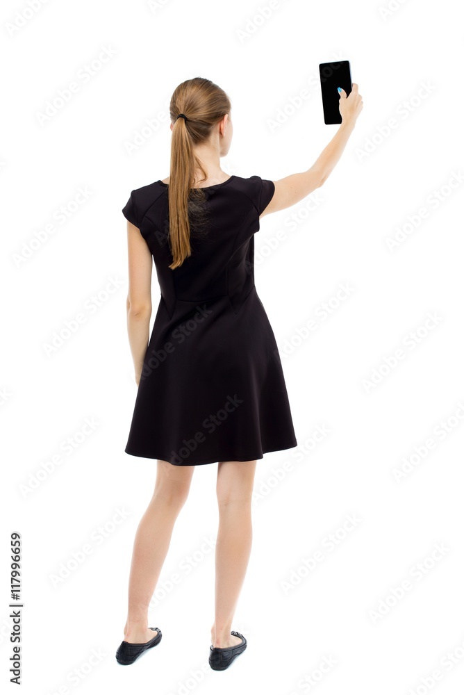 back view of standing young beautiful girl with tablet computer in the hands of. girl watching. Rear view people collection. backside view of person. Isolated over white background.The blonde in a back view of standing young beautiful girl with tablet computer in the hands of. girl watching. Rear view people collection. backside view of person. Isolated over white background.The blonde in a