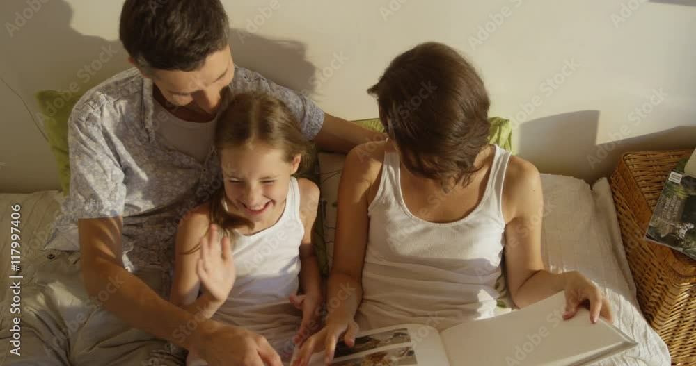 Mother, father and daughter wearing pajamas reading a book together laying in bed Mother, father and daughter wearing pajamas reading a book together laying in bed