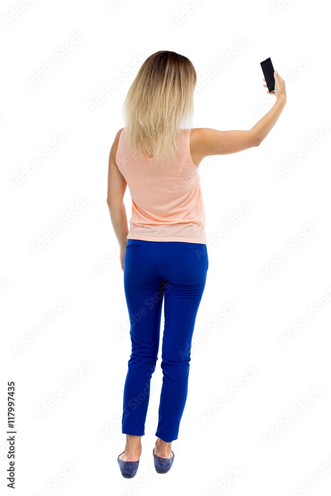 back view of standing young beautiful woman and using a mobile phone. girl watching. Rear view people collection. backside view of person. Isolated over white background. Blonde in blue pants back view of standing young beautiful woman and using a mobile phone. girl watching. Rear view people collection. backside view of person. Isolated over white background. Blonde in blue pants