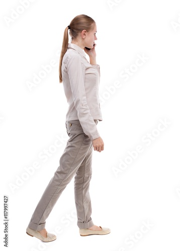 side view of a woman walking with a mobile phone. back view ofgirl in motion. backside view of person. Rear view people collection. Isolated over white background. A girl in a white jacket walking