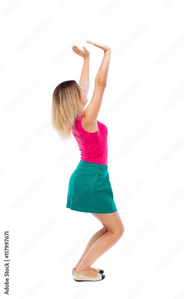 back view of woman pushes wall. Isolated over white background. Rear view people collection. backside view of person.The blonde in a green skirt and pink blouse sitting down holding something heavy back view of woman pushes wall. Isolated over white background. Rear view people collection. backside view of person.The blonde in a green skirt and pink blouse sitting down holding something heavy