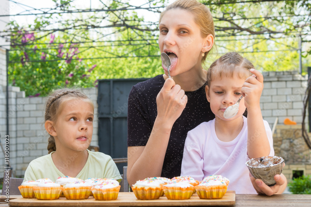 Mother and two daughters lick spoons with confectionery icing for Easter cupcakes
