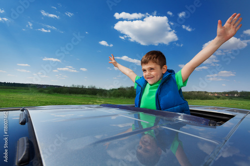 Smiling kid boy enjoying freedom on sunroof of car photo