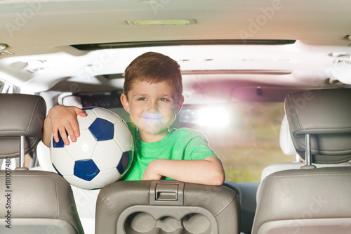 Smiling kid boy holding soccer ball inside the car