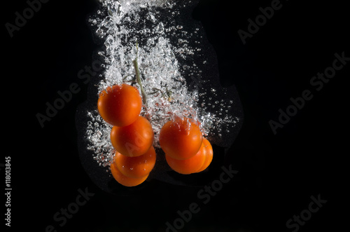 The branch of cherry tomatoes in water splash with bubbles on a black background.