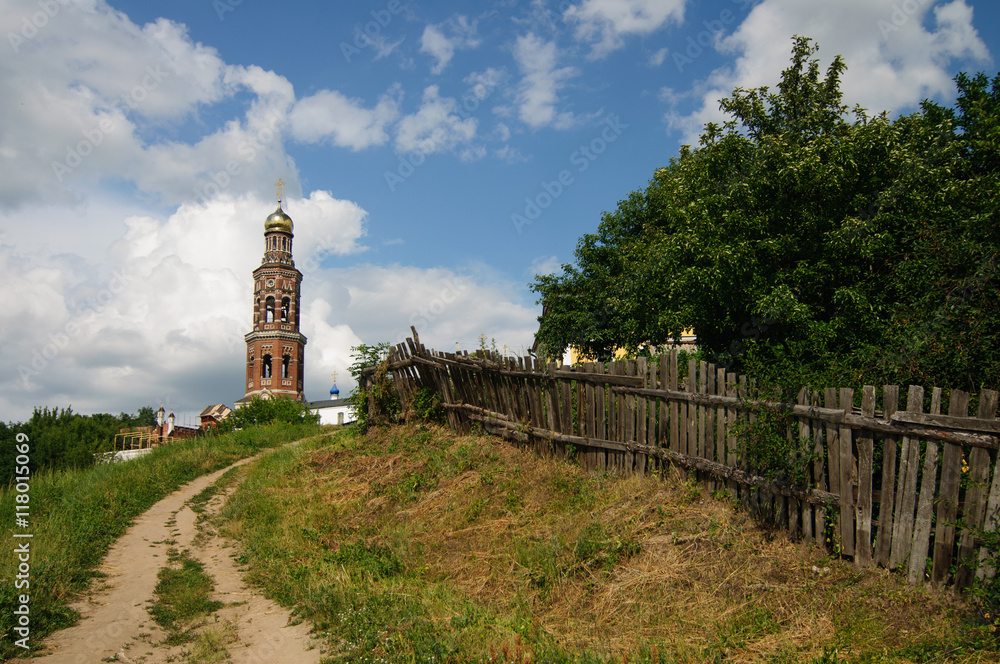 Грунтовая дорога, ведущая к православному храму вдоль деревянного забора 