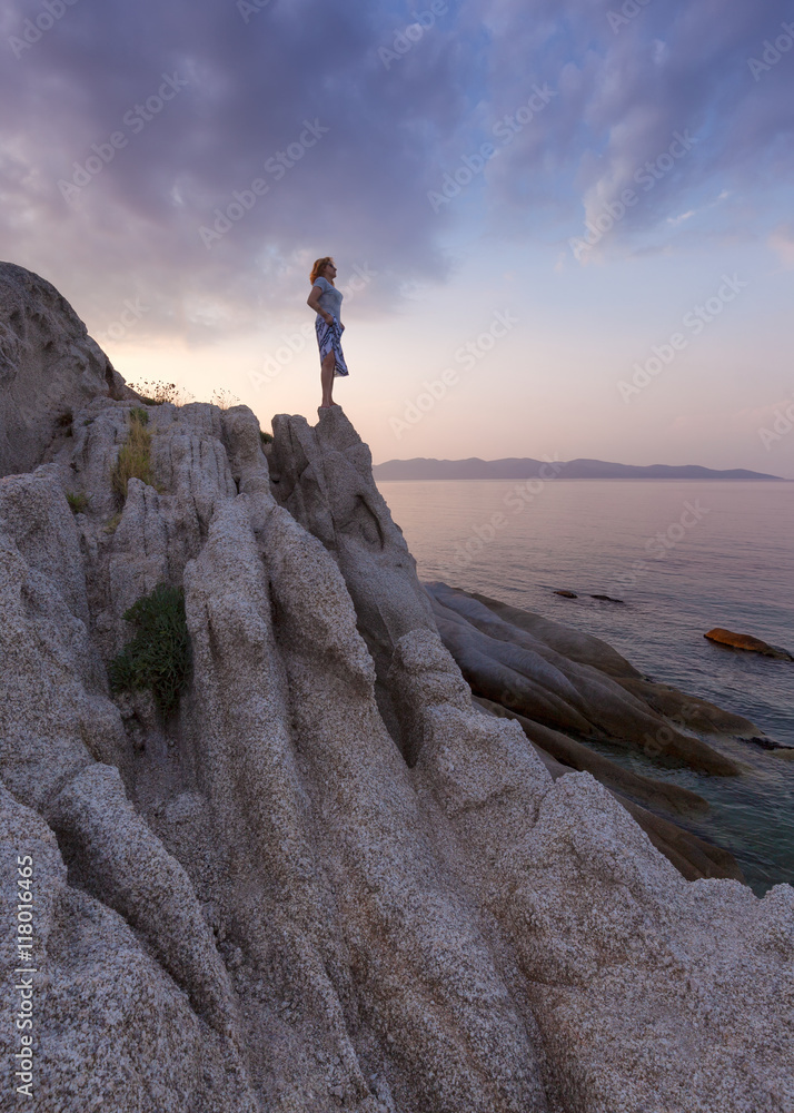 Solitude girl watching sunset high up on cliff by sea