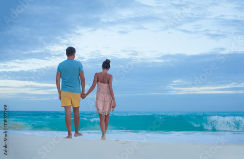 couple in bright clothes walking at the tropical beach in the evening