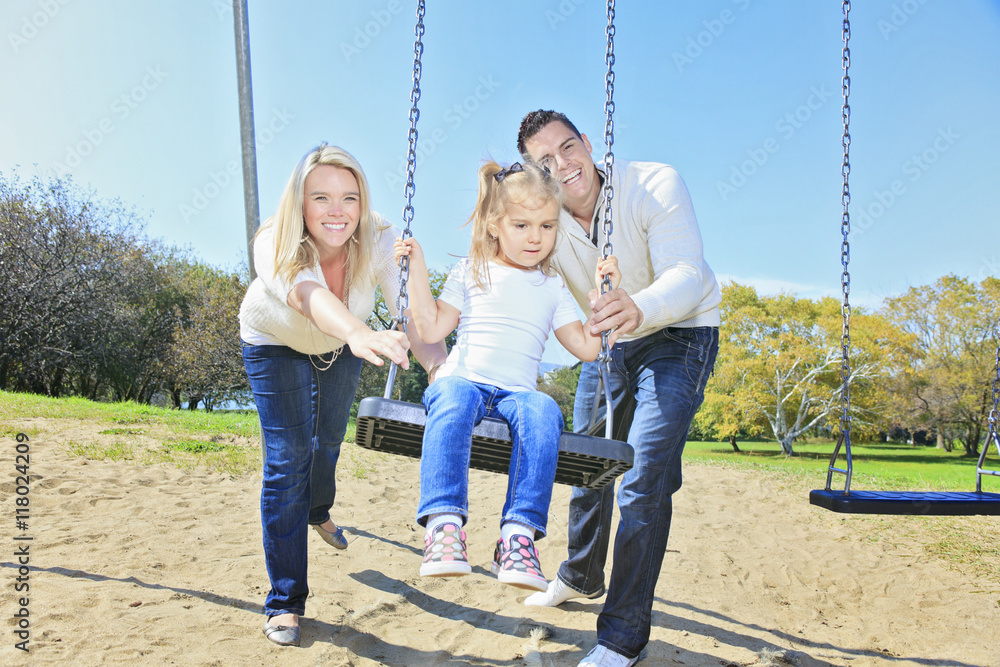 Girl sitting on a swing, father on mother pushing