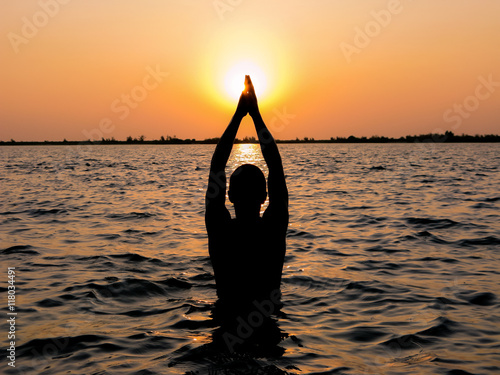 A man in meditation and prayer as he stand in a holy river at dusk. photo