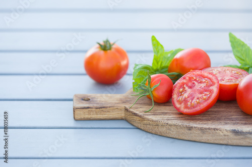 Fresh organic tomatoes with basil on wooden board on grey table. Healthy food concept