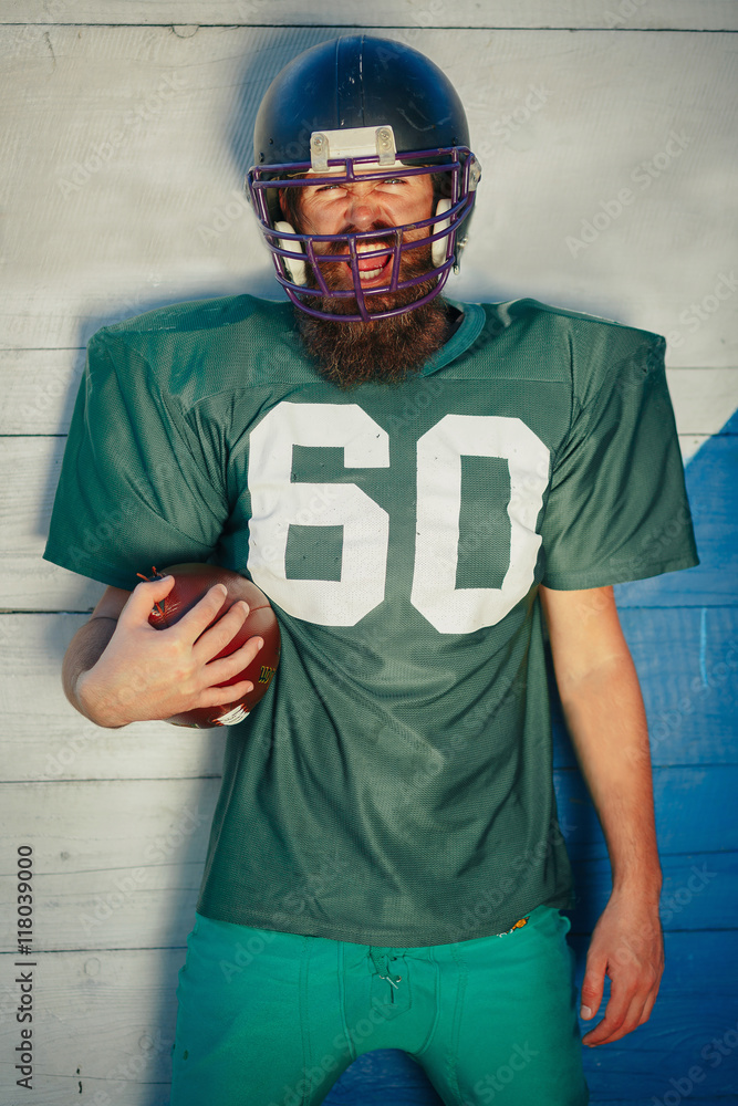 Brutal man with a long beard and mustache in the shape of an American  football player with helmet and Ball on the training ground Stock Photo