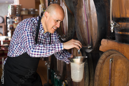 Happy mature man seller pouring wine from wood