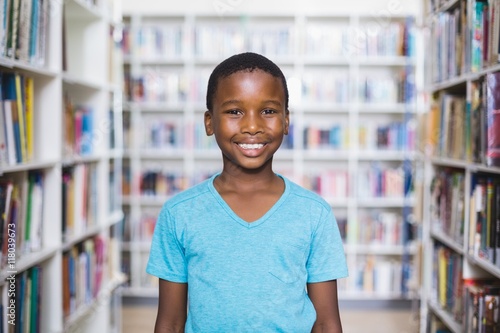 Happy schoolboy standing in library