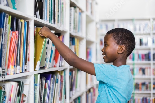 Canvas Print Schoolboy selecting a book from bookcase in library