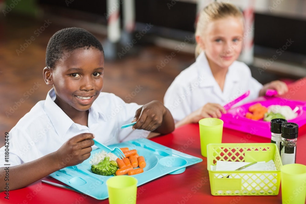 Boy and girl in school uniforms having lunch in school cafeteria Photos
