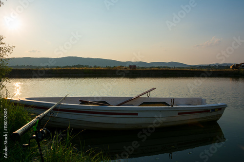 Fishing rod on white wooden rowing boat on a beautiful fishing lake at sunset