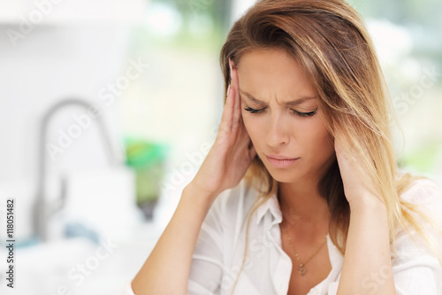 Young sad woman suffering from headache in kitchen photo