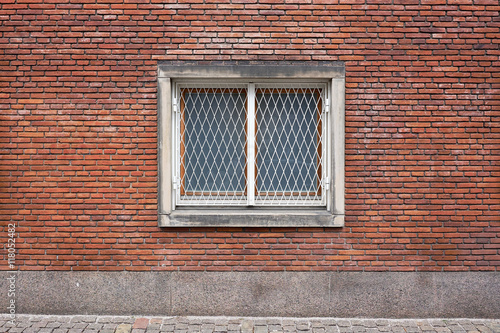 Closed double casement window with matte glazing and a metal grill for protection, placed in red brick facade wall in Frederiksberg City Hall, Denmark