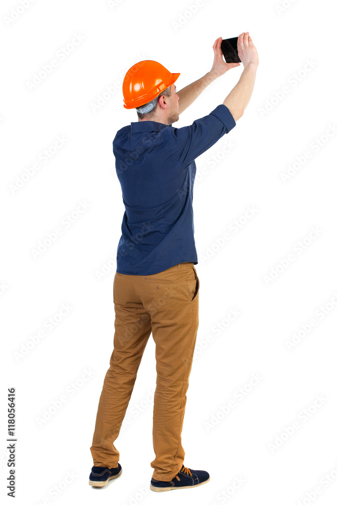 Backview of business man in construction helmet stands and enjoys tablet or using a mobile phone. Standing young guy. Rear view people collection. backside view of person. Isolated over white Backview of business man in construction helmet stands and enjoys tablet or using a mobile phone. Standing young guy. Rear view people collection. backside view of person. Isolated over white