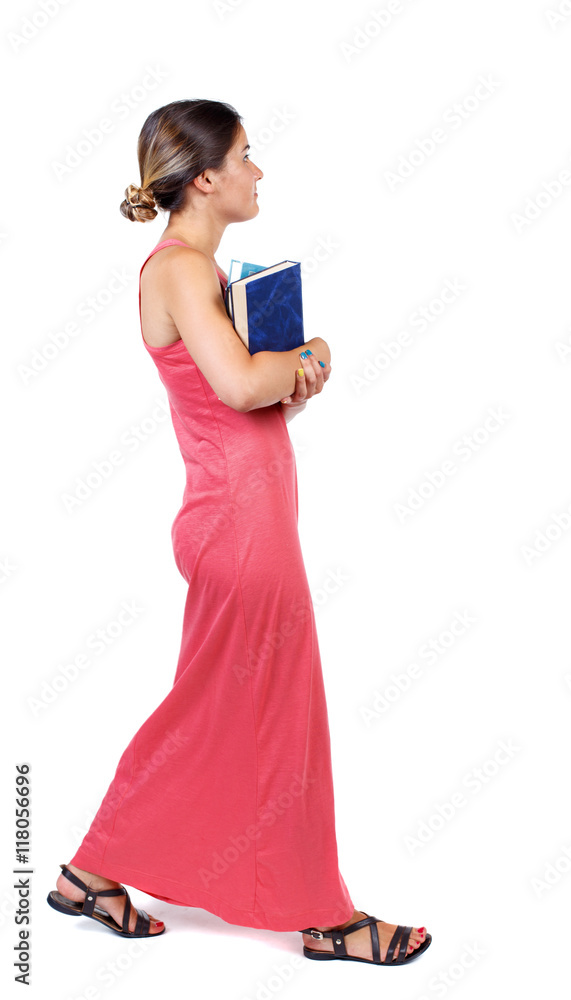 Girl comes with stack of books. side view. Rear view people collection. backside view of person. Isolated over white background. A slender woman in a long red dress goes on the side carrying the Girl comes with stack of books. side view. Rear view people collection. backside view of person. Isolated over white background. A slender woman in a long red dress goes on the side carrying the